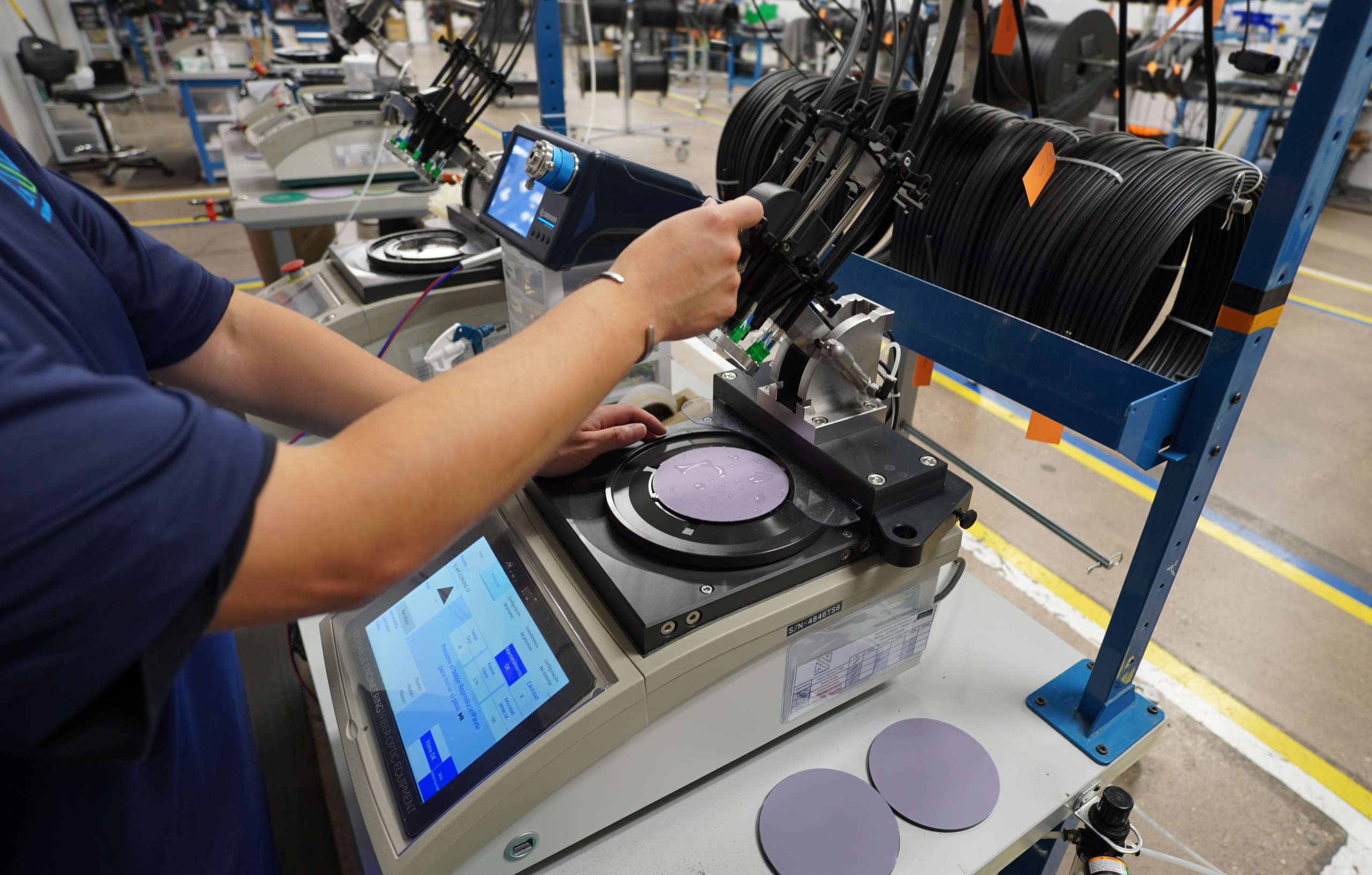 Technician polishing fiber optic connectors at a NetSource OEM cable assembly workstation.